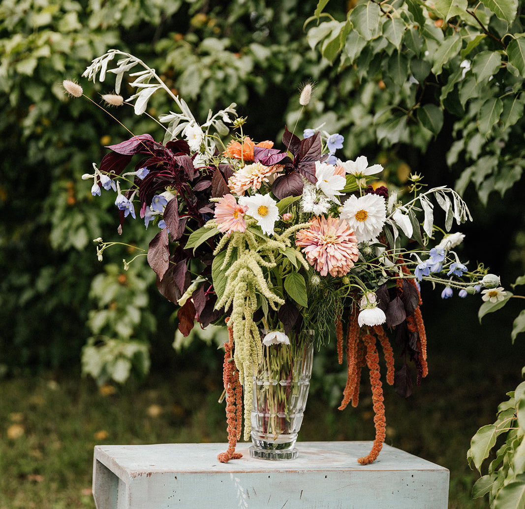 Floral arrangement in a glass vase on a wooden table with greenery in the background
